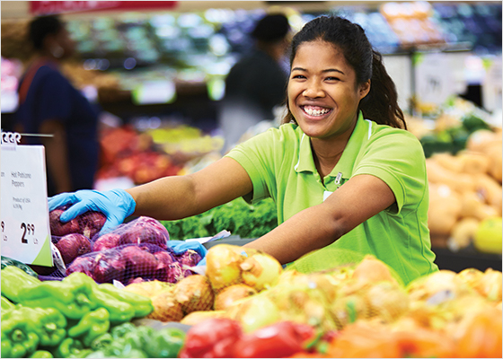 Une employée de FreshCo dépose des oignons sur une table de fruits et légumes.