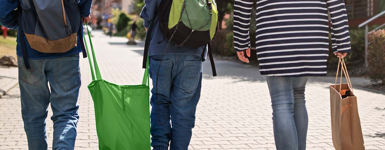 Une mère marche avec deux jeunes garçons qui transportent des sacs réutilisables.